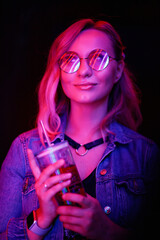 Modern young woman in glasses and denim coat . Confident female model in iridescent multicolors of lighting. Neon. Disco light