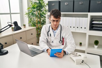 Young hispanic man doctor using laptop and touchpad working at clinic