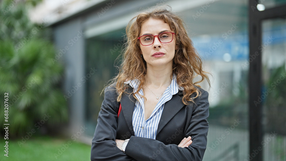 Wall mural Young woman business worker standing with arms crossed gesture and serious face at street