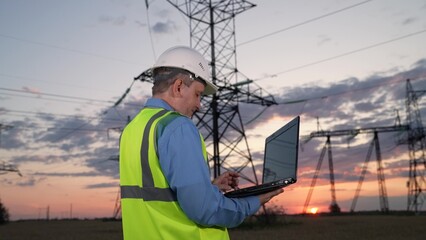 Fototapeta na wymiar Mature manager sets up power transmission lines equipment via laptop in evening