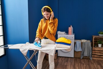 Young blonde woman listening to music ironing clothes at laundry room