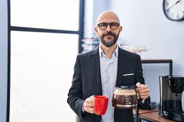 Young bald man business worker holding cup and jar of coffee at office