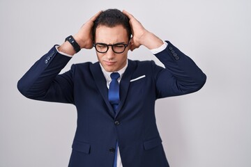 Young hispanic man wearing suit and tie suffering from headache desperate and stressed because pain and migraine. hands on head.