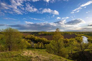 View from the hill to plowed farmland. Landscape with a river, arable land and green trees.