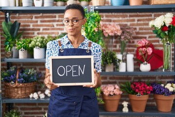 African american woman working at florist holding open sign smiling looking to the side and staring...