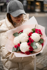 Large bouquet of white chrysanthemums with small roses in a wrapper is held by a woman