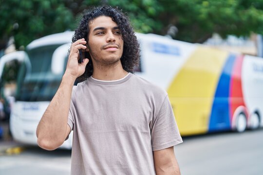 Young latin man talking on smartphone with serious expression at bus station