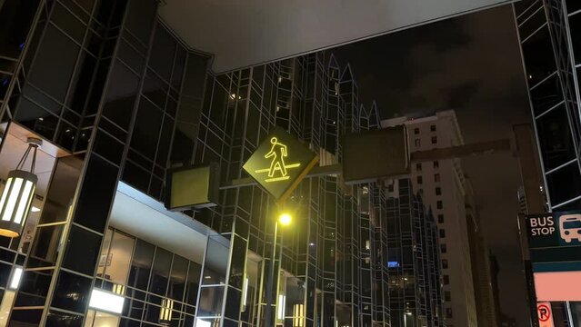A night low angle view of a flashing pedestrian crossing warning sign in the downtown area of a large city.  	
