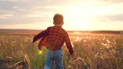 Active boy runs along field of cultivated plants in countryside at sunset