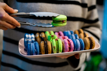 Female hands hold a set of colorful macaroons and in the other hand one macaroon with kitchen tongs
