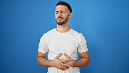 Young arab man suffering for stomach ache standing over isolated blue background