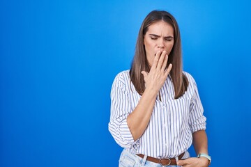 Hispanic young woman standing over blue background bored yawning tired covering mouth with hand....