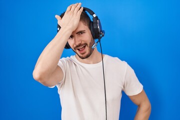 Hispanic man with beard listening to music wearing headphones surprised with hand on head for...