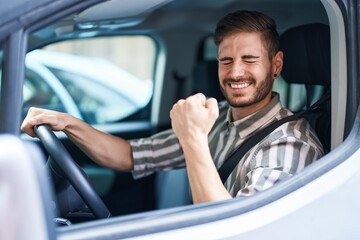 Hispanic man with beard driving car screaming proud, celebrating victory and success very excited with raised arm