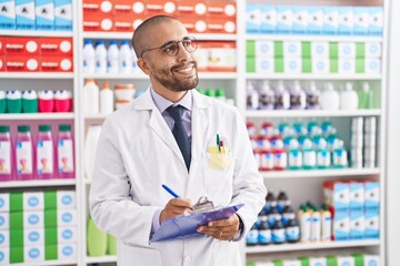 Young latin man pharmacist writing on document at pharmacy