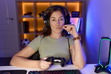 Beautiful brunette woman playing video games wearing headphones mouth and lips shut as zip with...