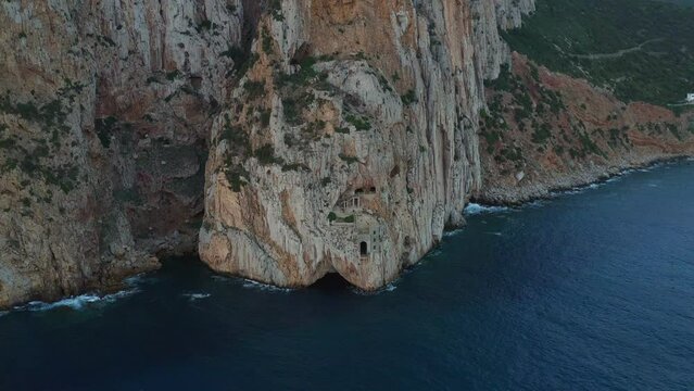 Aerial drone view of Porto Flavia mines entrance on the rocks in Sardinia at sunset, Italy