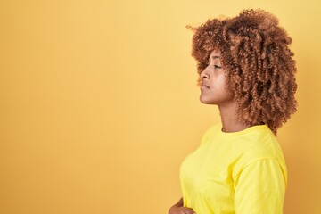 Young hispanic woman with curly hair standing over yellow background looking to side, relax profile...