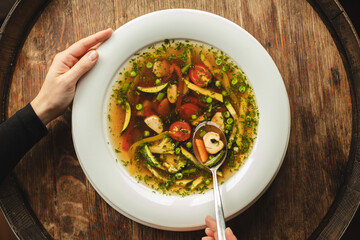 A plate of soup with vegetables on a wooden background. First course, delicious broth.