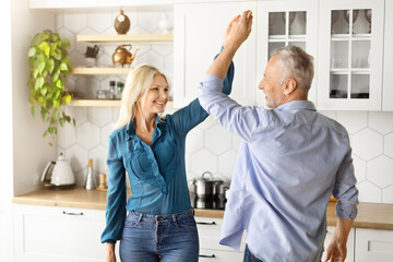 Portrait Of Cheerful Older Couple Dancing Together In Kitchen Interior