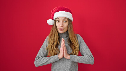 Young caucasian woman smiling praying wearing christmas hat over isolated red background