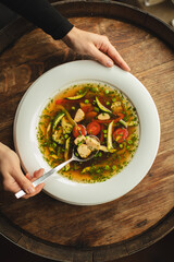 A plate of soup with vegetables on a wooden background. First course, delicious broth.