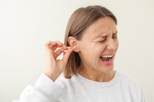 Young woman enjoys to using disposable cotton bud, swab, stick for cleans her auricle earwax on white background. Personal hygiene and care product. Prevention of ear diseases. Sulfur plug removal.