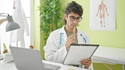 Young hispanic man doctor writing medical report thinking at clinic