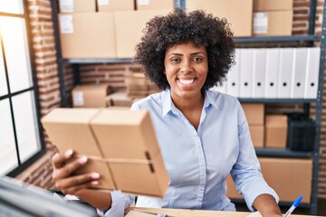 African american woman ecommerce business worker writing on notebook holding package at office