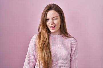 Obraz premium Young caucasian woman standing over pink background winking looking at the camera with sexy expression, cheerful and happy face.