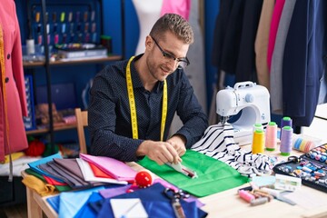 Young caucasian man tailor smiling confident make mark on cloth at clothing factory