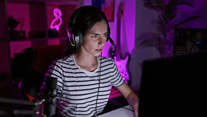 Young beautiful hispanic woman streamer wearing headset playing video game at gaming room