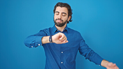 Young hispanic man looking watch over isolated blue background