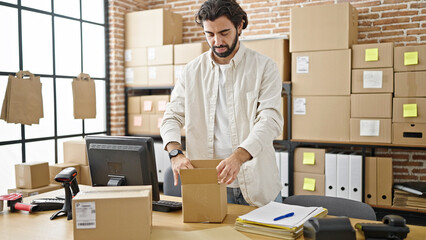Young hispanic man ecommerce business worker packing cardboard box at office