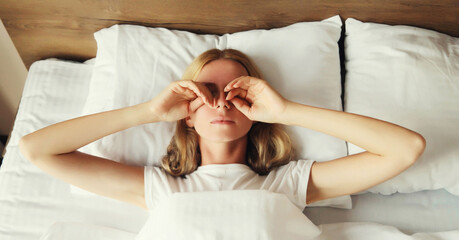 Upset sad woman wakes up covering her eyes with her hands lying on the bed on pillow while...