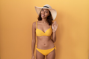 Young hispanic woman wearing bikini and summer hat waiving saying hello happy and smiling, friendly welcome gesture © Krakenimages.com