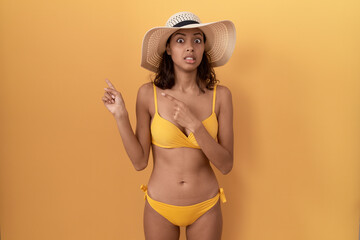 Young hispanic woman wearing bikini and summer hat pointing aside worried and nervous with both...