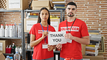 Man and woman volunteers standing together holding thank you paper at charity center