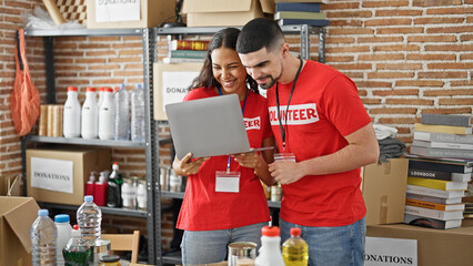 Man and woman volunteers smiling, working on laptop at charity center, standing together in service for community