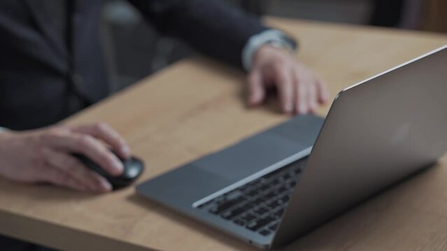 Man clicks the mouse on the laptop screen and starts gesturing with his hands. Person sits at a desk in the office and consults. Businessman at work or making a deal.