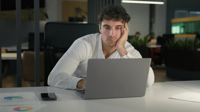 Tired exhausted Caucasian businessman bored fatigued male designer with computer project sad overworked overtime working at creative modern office business man employer work laptop boring deadline