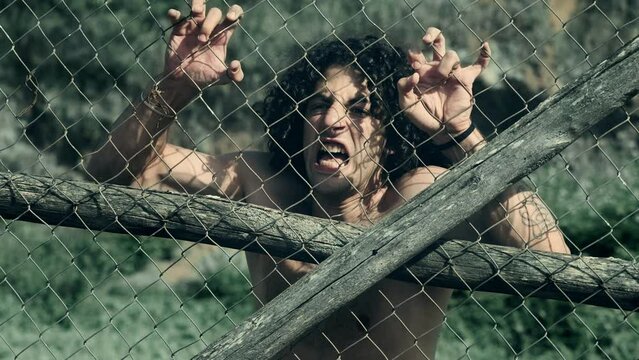 A young man's fervent efforts to break free from behind a mesh barrier symbolize the conceptual theme of imprisonment and confinement.