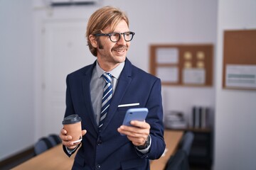 Young blond man business worker using smartphone drinking coffee at office
