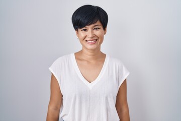 Young asian woman with short hair standing over isolated background with a happy and cool smile on...