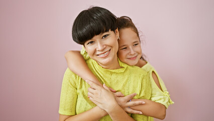 Confident mother and daughter sharing a lovely, happy hug while smiling and standing together over an isolated pink background, expressing a casual lifestyle full of fun, joy and positive vibes.