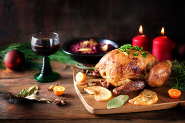 Festive roast chicken with red cabbage, citrus fruits, herbs and wine on a dark rustic wooden board...