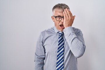 Hispanic business man with grey hair wearing glasses covering one eye with hand, confident smile on face and surprise emotion.