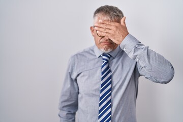 Hispanic business man with grey hair wearing glasses covering eyes with hand, looking serious and sad. sightless, hiding and rejection concept