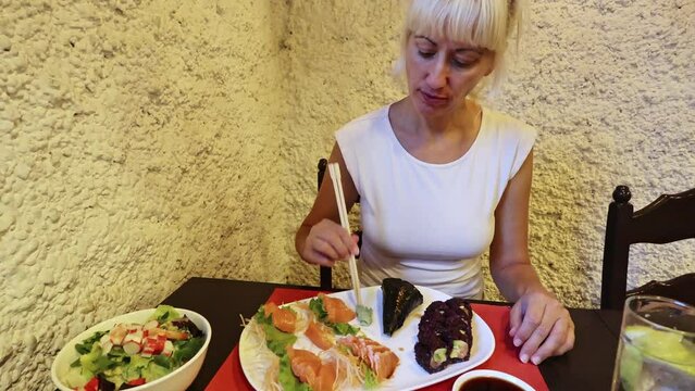 glamour lady eating salmon sashimi and Uramaki rools with chopsticks. In Japanese Asian fusion restaurant. Healthy food, light diet concept. Happy woman eating japanese food. healthy diet of fresh