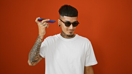 Confident young latin man with a cool tattoo, standing casually over a purely red isolated...